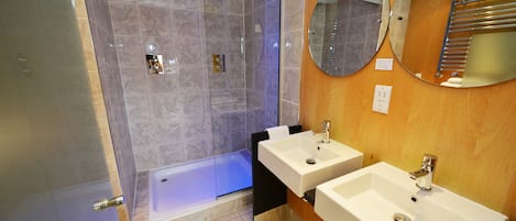 A modern bathroom with a glass-enclosed shower, a bathtub, and two sinks.