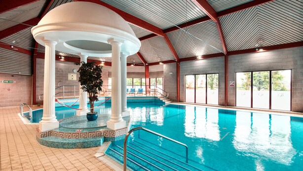 Una piscina interior con una columna central, escalones que bajan a la piscina y un techo con diseño en chevron.