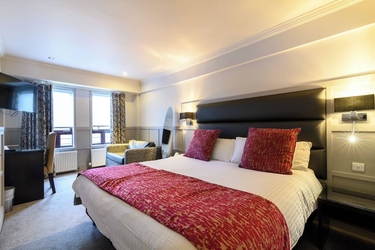 A hotel room with a large bed, a desk, a chair, and a view of the outdoors.