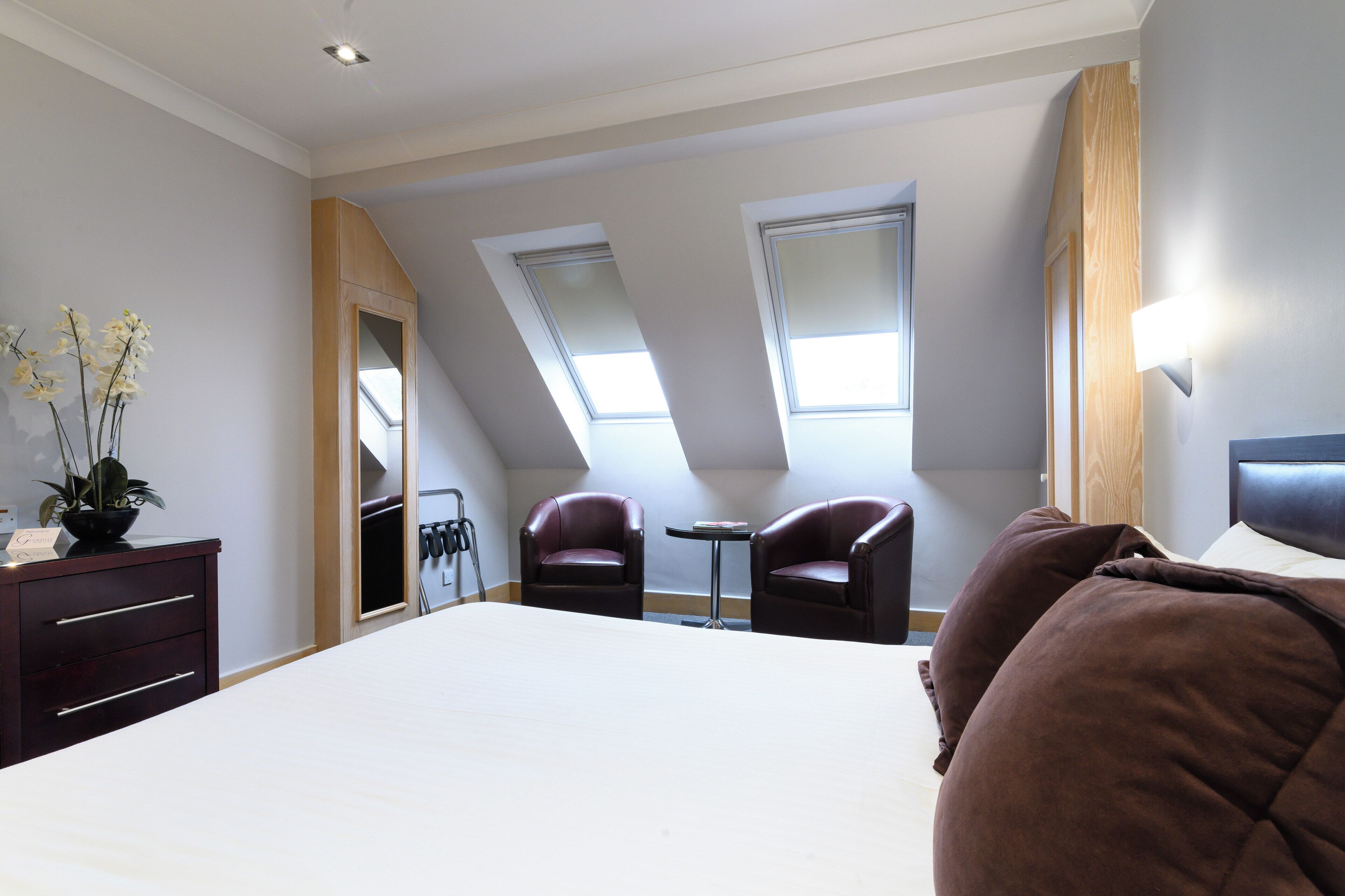 A bedroom with a large bed, two leather chairs, a small table, and a dresser. There are skylights on the ceiling.