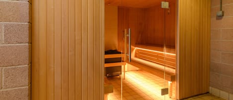 Ein Saunaraum mit Holztür, Sitzbank und gefliestem Boden.