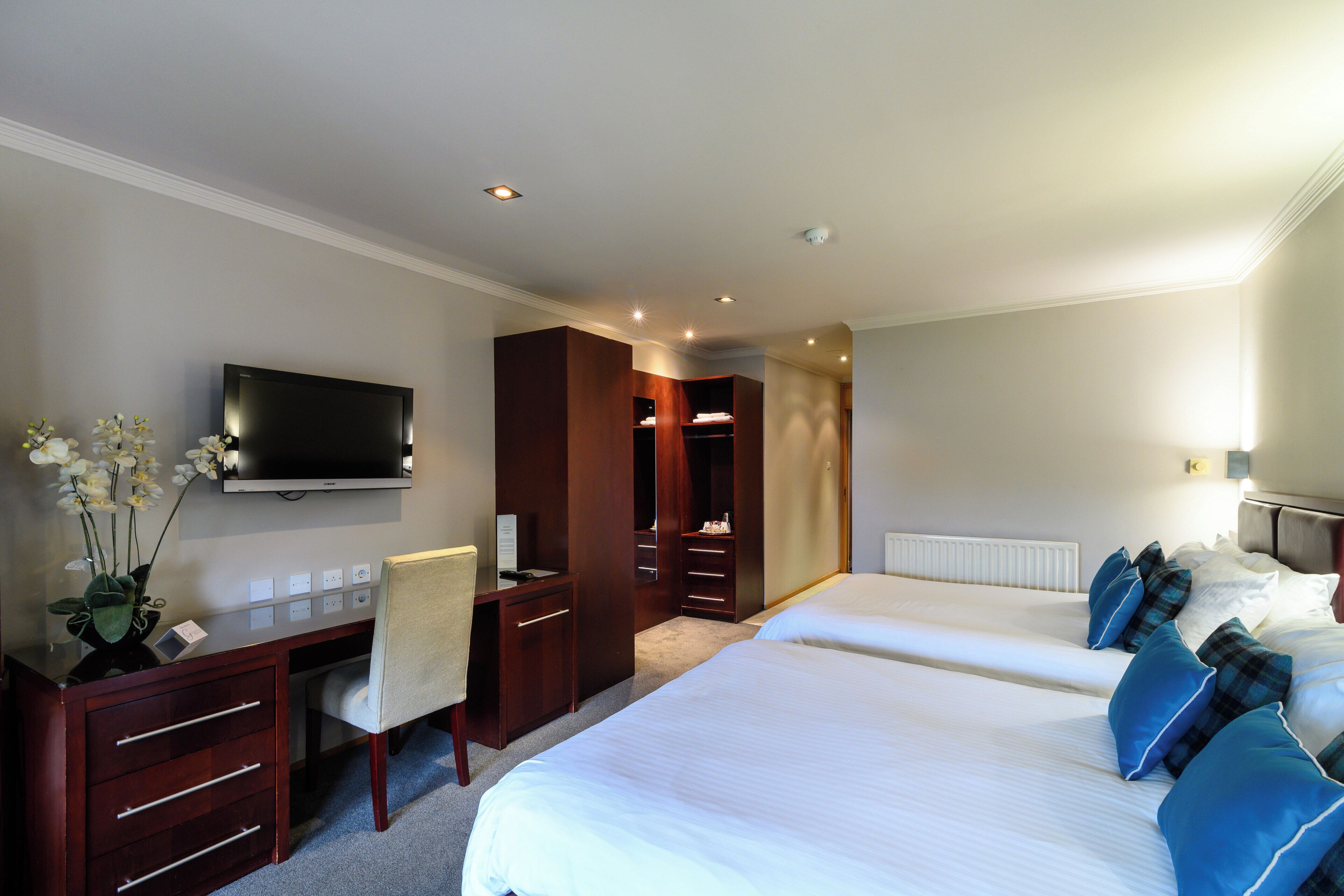 A hotel room with a bed, a desk, a chair, a television, and a wardrobe.