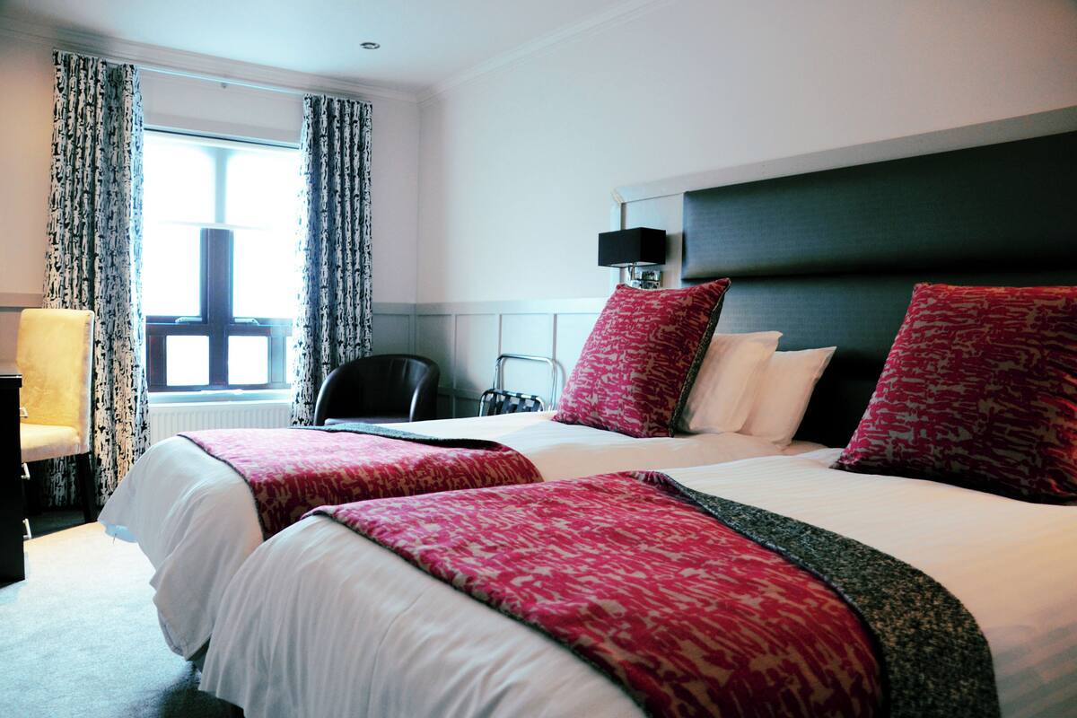 A hotel room with two beds, a chair, a desk, and a window with curtains.