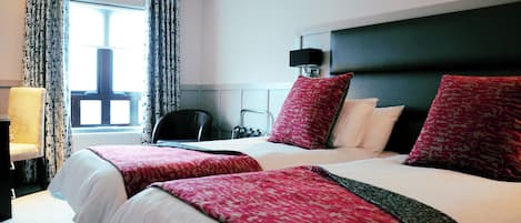 A hotel room with two beds, a chair, a desk, and a window with curtains.