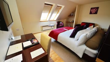 Habitación de hotel con cama, escritorio, silla y una mesita. Dos ventanas permiten la entrada de luz natural.