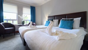 Habitación de hotel con dos camas, una silla y un ventanal con cortinas.