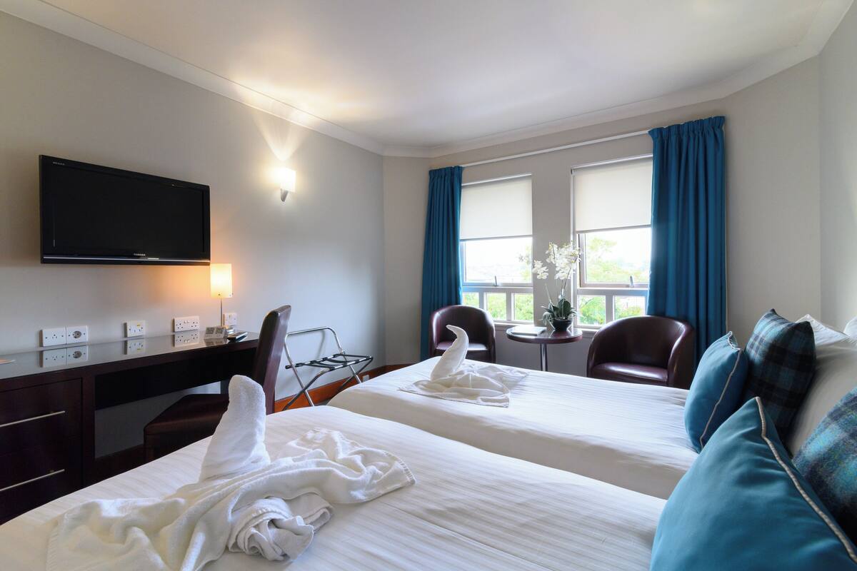 A hotel room with two beds, a desk, a chair, a television, and a window with curtains.