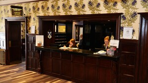 Una recepción con detalles de madera, un fondo de papel tapiz estampado y un cartel que indica Palm Court Carvery y Harry's Bar.
