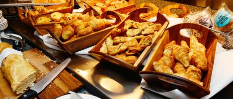 A buffet with various baked goods including bread, pastries, and muffins.