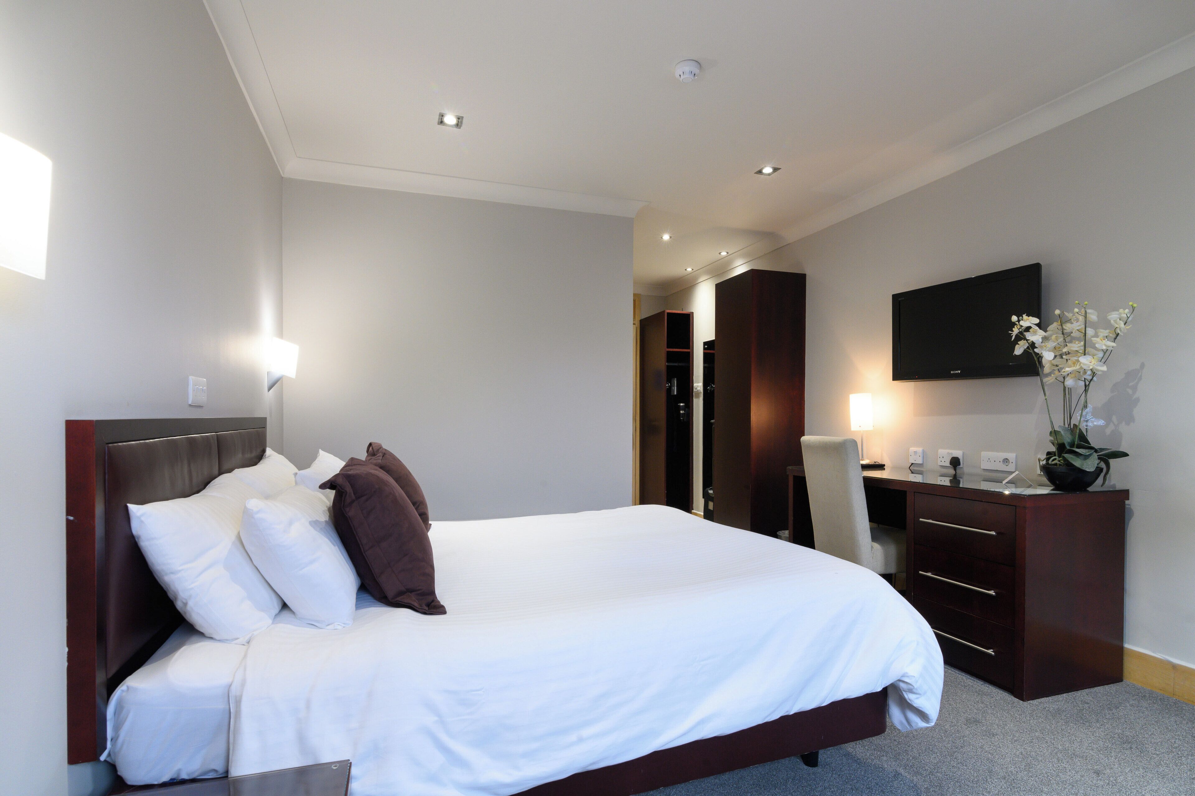 A hotel room with a large bed, a desk with a chair, a television, and a plant.
