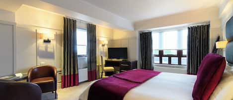 A hotel room with a bed, a desk, a chair, a TV, and curtains.