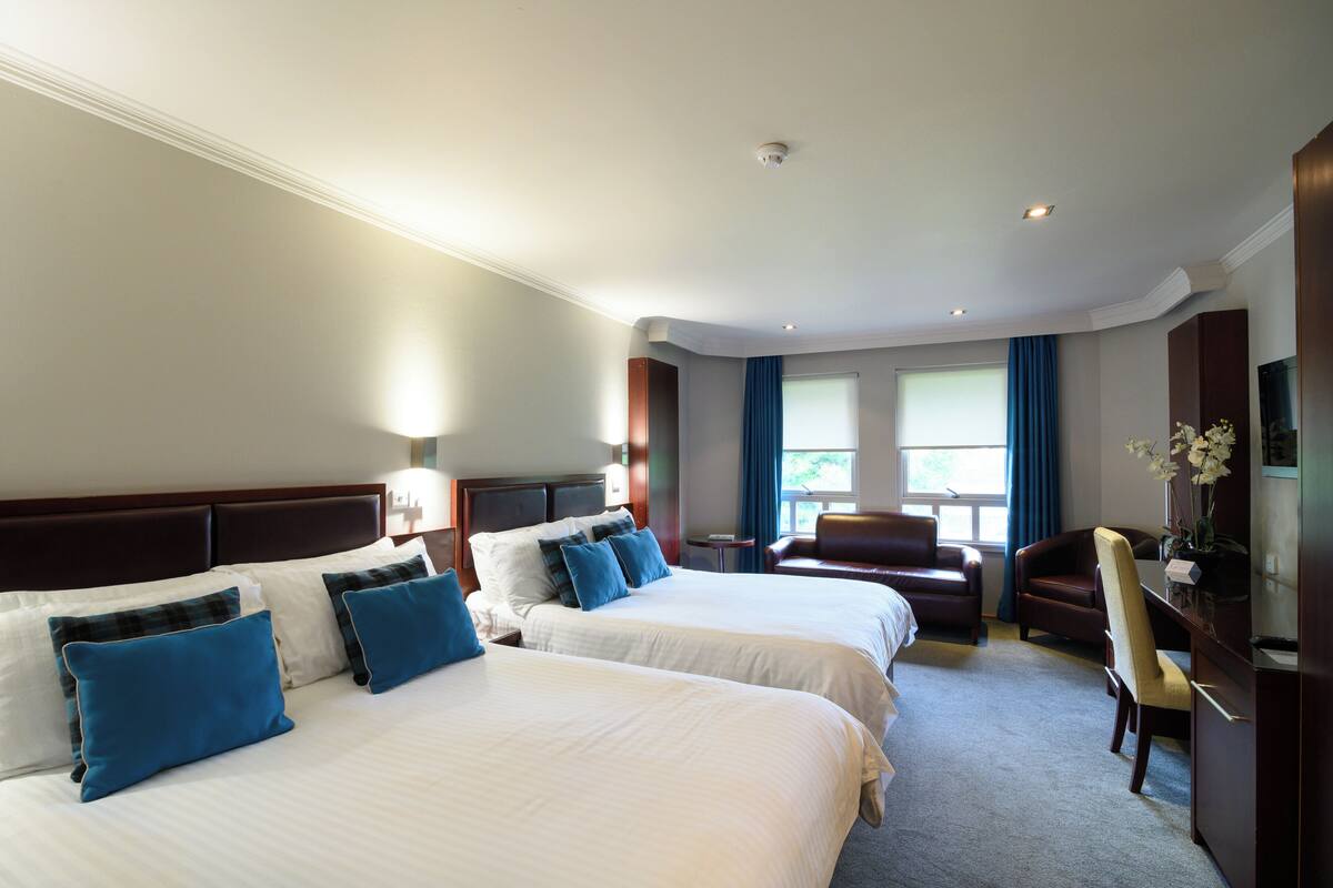 A hotel room with two beds, a desk, a chair, and a television.