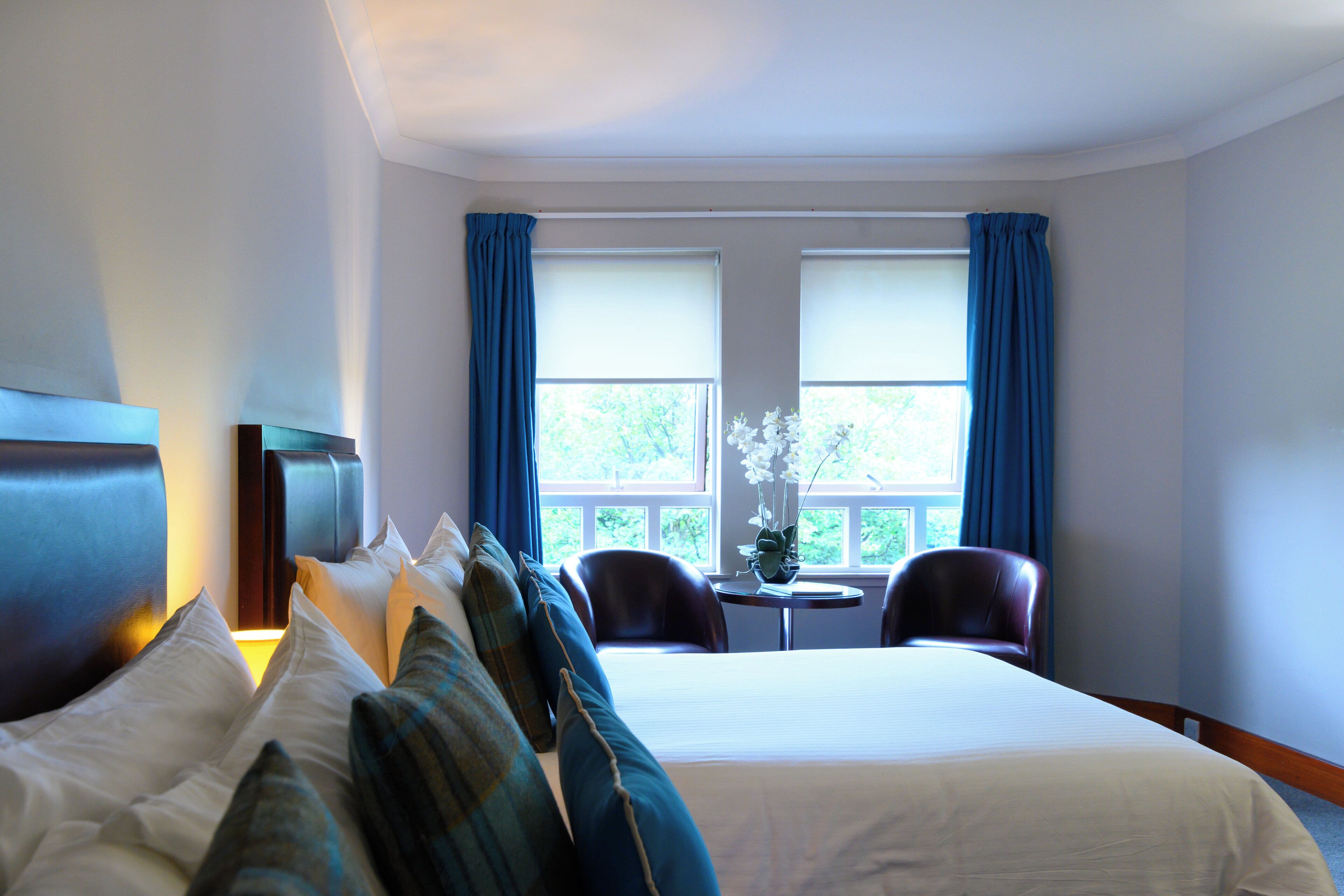 Habitación de hotel con una cama grande, dos sillones, una mesita y un televisor.
