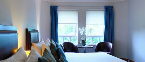 A hotel room with a large bed, two chairs, a small table, and a TV.