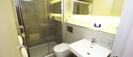 Un bany modern amb dutxa de vidre, un lavabo blanc i un vàter.