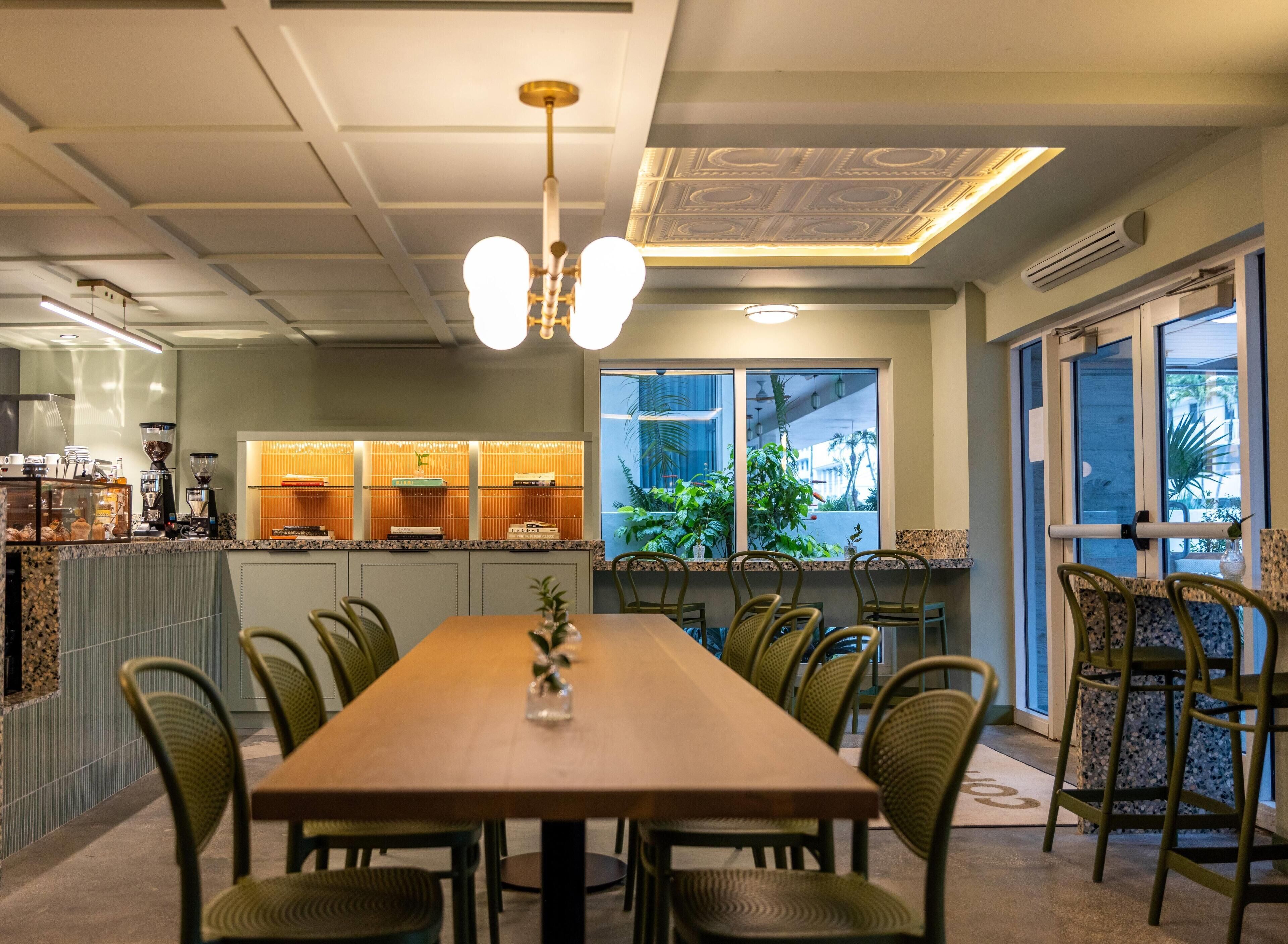 Een restaurant met een lange houten tafel, groene stoelen en een plafond met decoratieve verlichting.