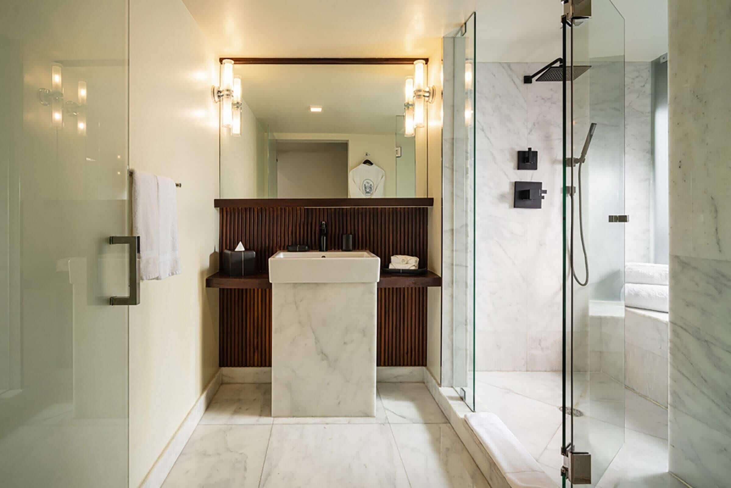 A modern bathroom with a glass shower enclosure, a marble sink, and wooden paneling.