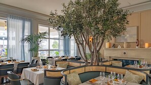 A restaurant with round tables, cushioned seating, and a large tree in the center.