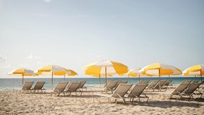 A beach with rows of sun loungers and yellow and white umbrellas.
