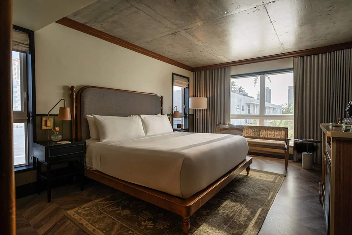 A spacious hotel room with a large bed, wooden headboard, and a view of the city through the window.