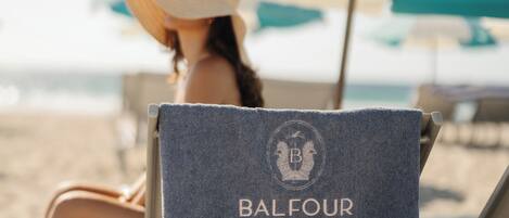 A beach chair with a towel labeled "Balfour" and a beach umbrella in the background.