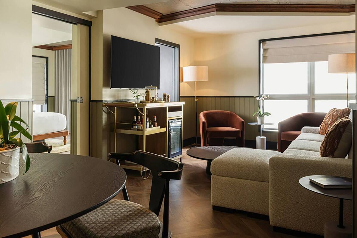A modern hotel room with a flat-screen TV, a dining table, a sofa, and a chair.