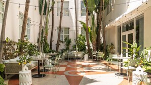 An indoor courtyard with tables and chairs, surrounded by tall palm trees and various plants.