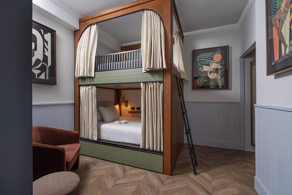 A room with a bunk bed, a chair, a lamp, and framed artwork on the walls.