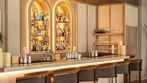 A bar area with a long counter, multiple shelves of bottles, and bar stools.