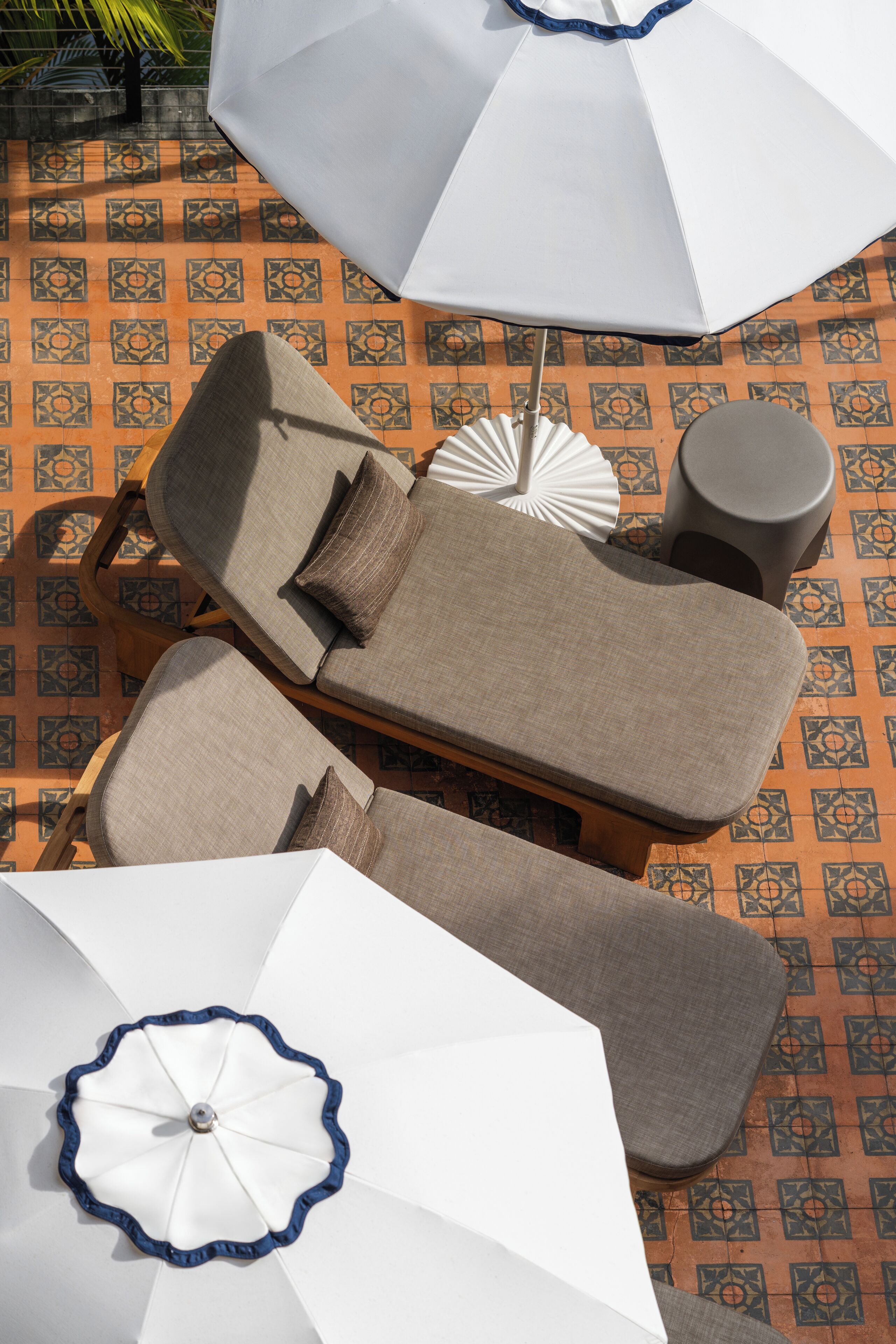 Un espace de détente ensoleillé comprenant deux chaises longues, une petite table ronde, un parasol et un ventilateur décoratif blanc.