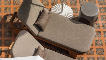 Un espace de détente ensoleillé comprenant deux chaises longues, une petite table ronde, un parasol et un ventilateur décoratif blanc.