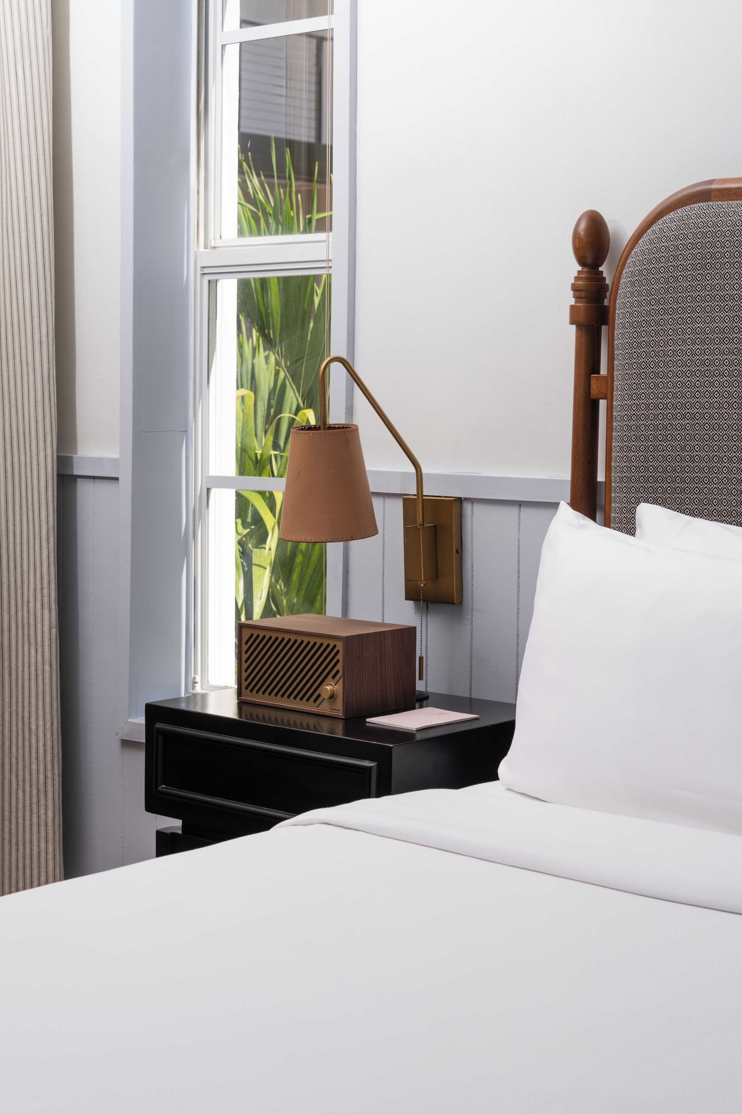A neatly made bed with white linens, a wooden headboard, and a bedside table with a lamp and radio.