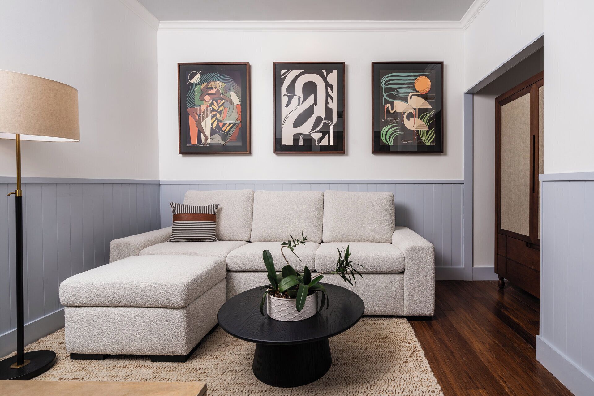 A living room with a sectional sofa, a round coffee table with a plant, and three framed artworks on the wall.