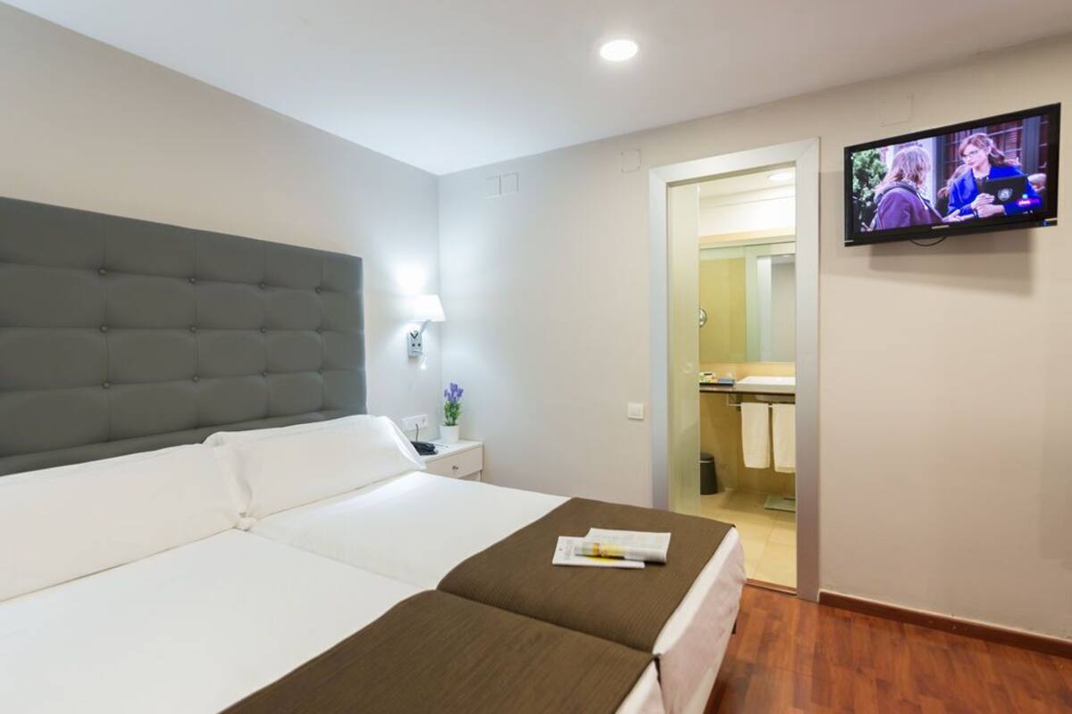 Une chambre d’hôtel avec un grand lit, un téléviseur fixé au mur et une salle de bain visible à travers une porte ouverte.