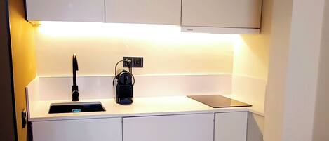 Cocina compacta con armarios blancos, encimera blanca, un lavamanos y una mesa redonda con una silla marrón.