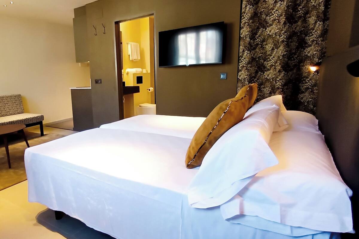 Une chambre d’hôtel avec un lit, un canapé, une petite table et un téléviseur fixé au mur.