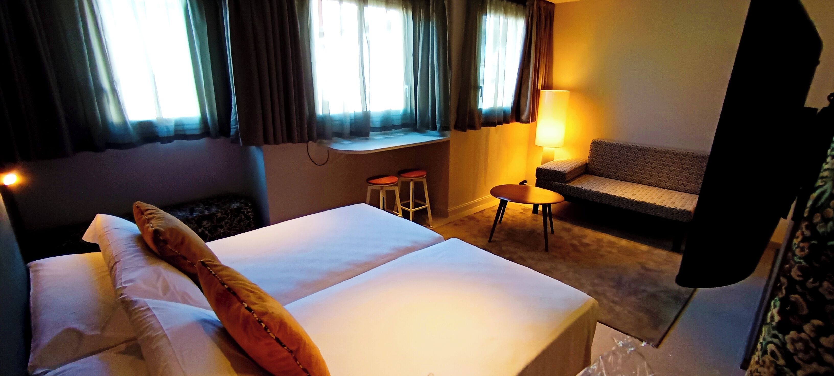 Una habitació d'hotel amb un llit, un sofà, una taula petita i una finestra amb cortines.