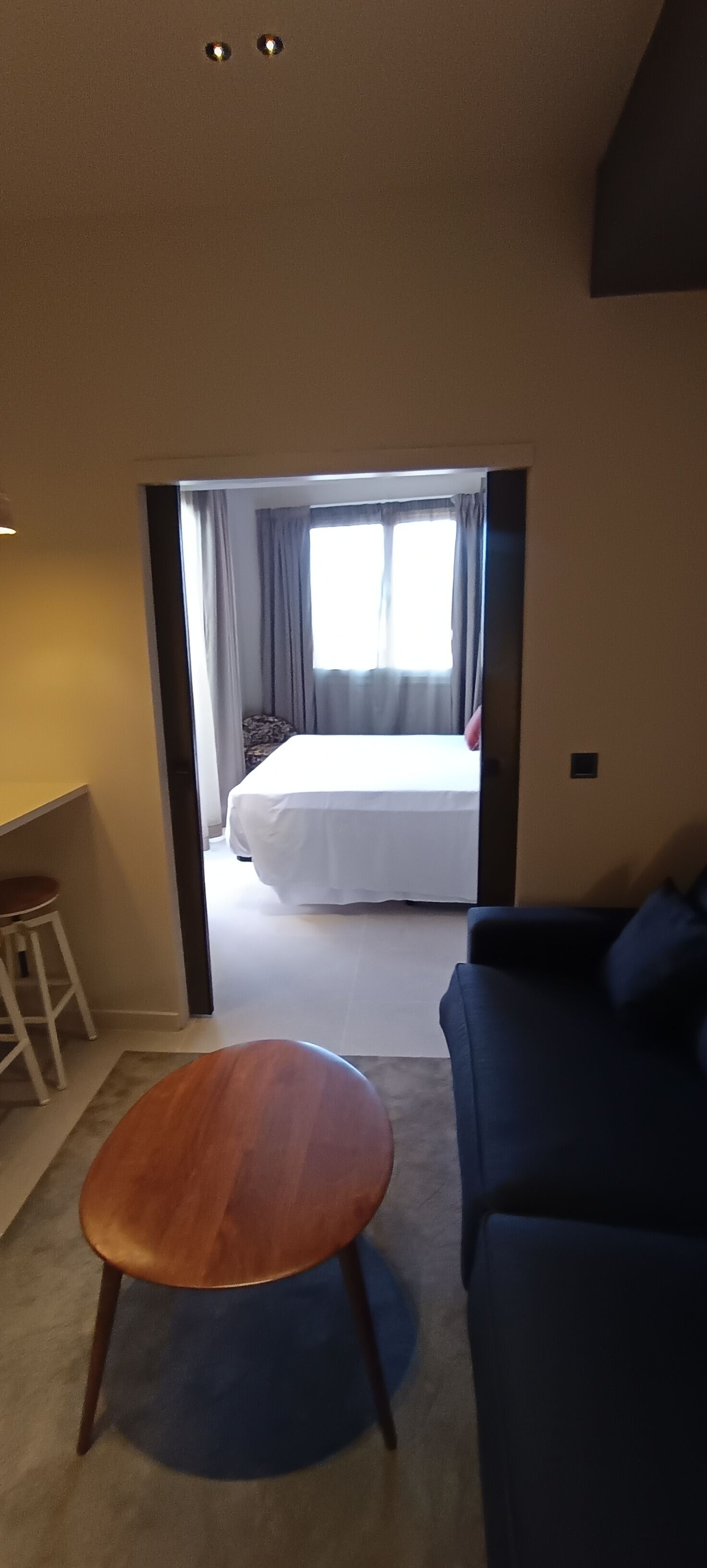 Una habitación de hotel con una cama, una silla de madera, un sofá azul y una ventana con cortinas.