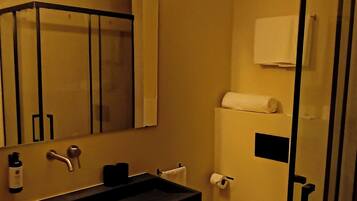 Un baño moderno con un lavabo negro, un espejo, un inodoro y una cabina de ducha de vidrio.