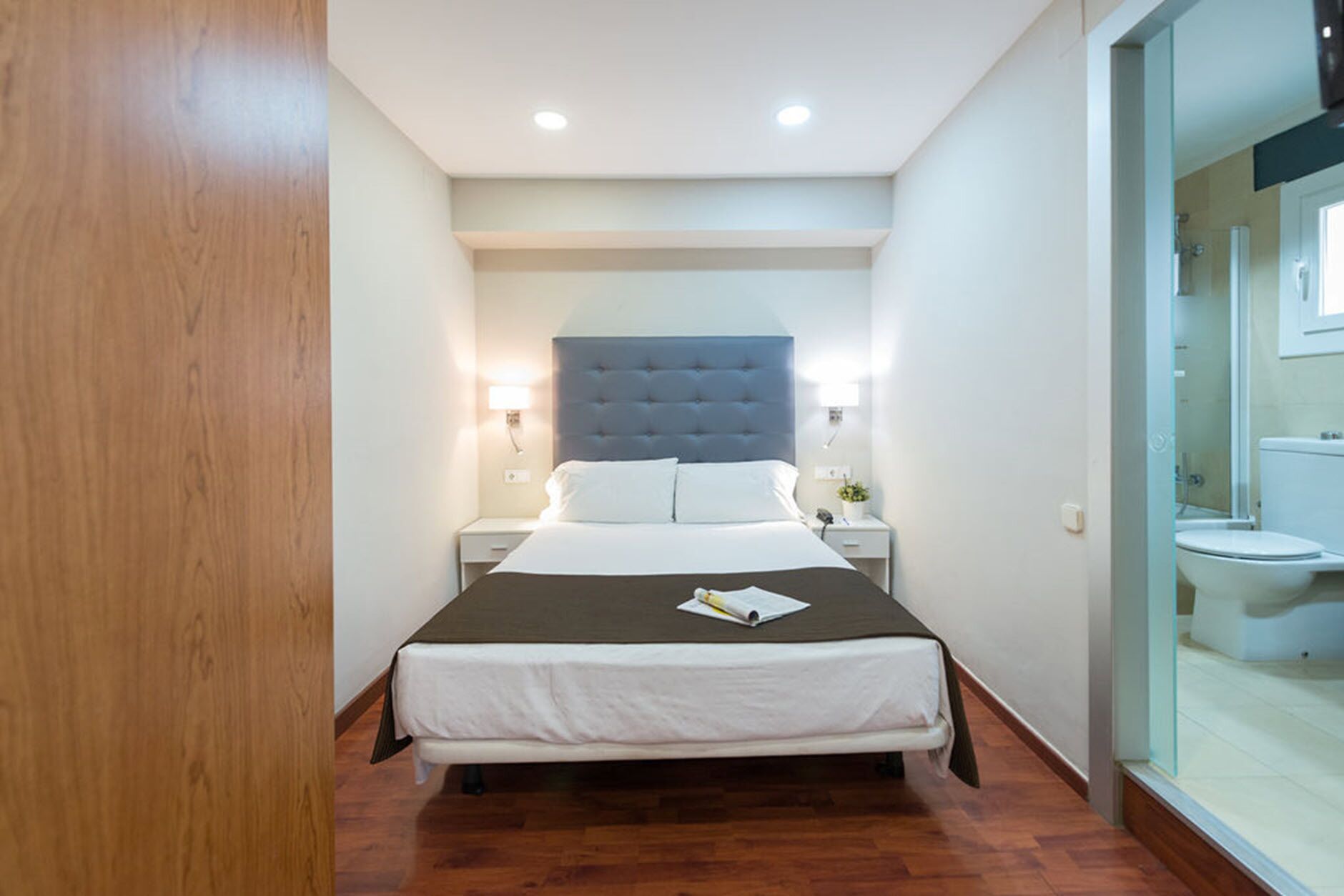 Hotelkamer met een groot bed, bedlampen, een houten vloer en uitzicht op de badkamer.