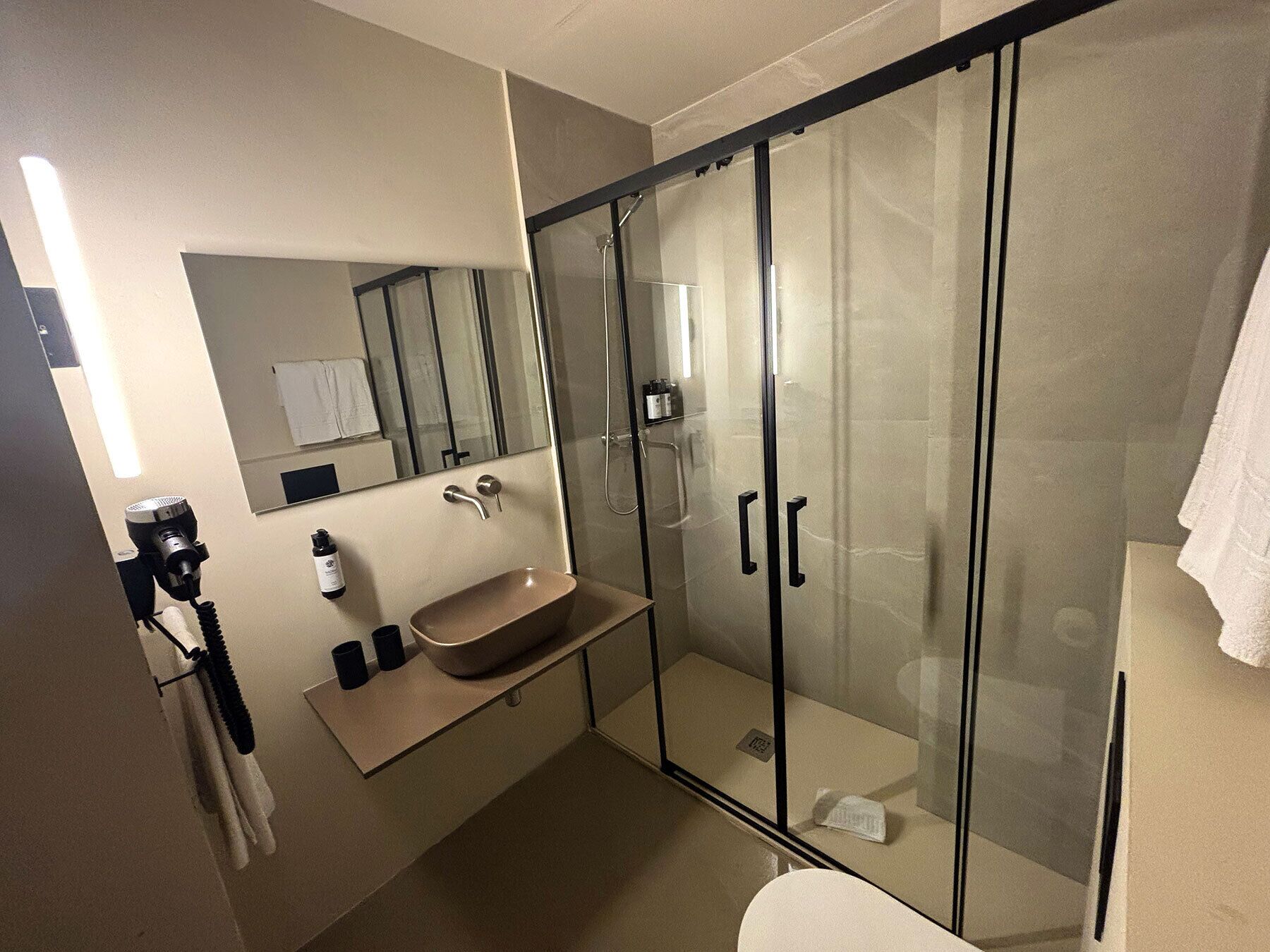 Ein modernes Badezimmer mit einer gläsernen Dusche, einem beigen Waschbecken und einem Spiegel darüber.