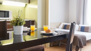 A hotel room with a dining area featuring a table, chairs, a potted plant, and breakfast items including a croissant and orange juice. - Senator Barcelona Apartments (Barcelona)
