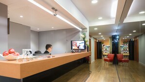 A reception area with a wooden reception desk, a television, and a seating area with red chairs. - Senator Barcelona Apartments (Barcelona)