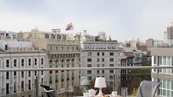 Ein Balkon mit zwei Stühlen und einem Tisch, mit Blick auf eine Stadtlandschaft mit historischen Gebäuden und einer Flagge.