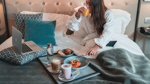 A hotel room with a bed, a laptop on a pillow, a tray with breakfast items, and a glass of orange juice. - Gran Hotel Havana by Escampa Hotels (Barcelona)