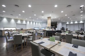 A modern dining area with multiple tables and chairs, a central counter, and a kitchen area in the background. - Gran Hotel Havana by Escampa Hotels (Barcelona)