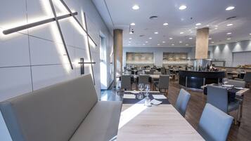 Un restaurante moderno con una larga mesa de comedor, asientos acolchados y una zona de cocina al fondo.
