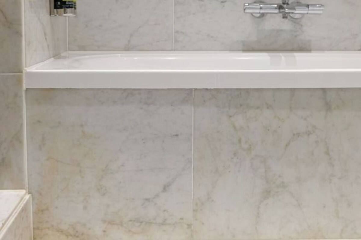 Un baño con una bañera blanca, un grifo cromado y baldosas de mármol.