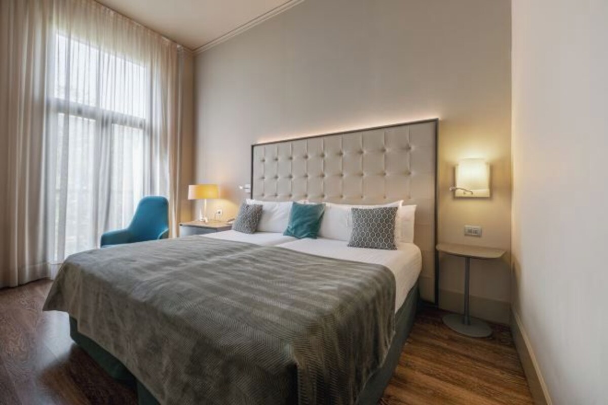 Una habitación de hotel con una cama, una silla, una mesita de noche y una lámpara.