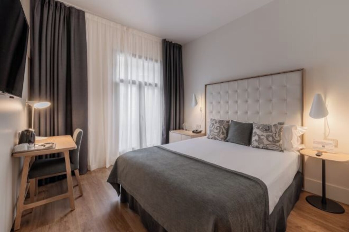 Una habitación de hotel con cama, mesita de noche, lámpara, silla y escritorio.